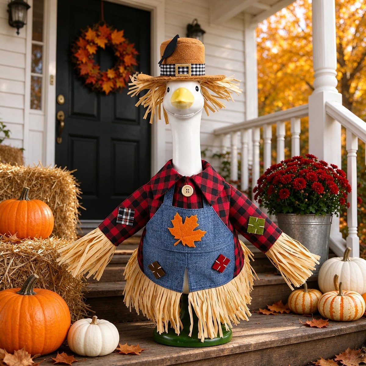 Porch goose wearing the plaid scarecrow outfit and crow hat beside autumn pumpkins